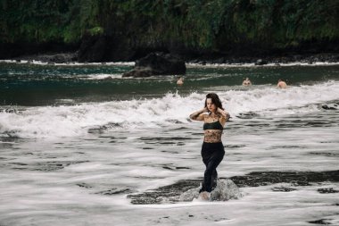 Dövmeli dişi, bereketli yeşillikler ve uzak plajlarda yaşayan kaygısız bir yaz atmosferini somutlaştıran sakin bir plajda okyanus dalgalarıyla şakalaşıyor.