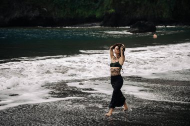 Kadın figürü kumlu sahilde yalın ayak yürüyor, dalgalar ayaklarına vuruyor, huzurlu bir sahil ortamında özgürlüğü ve huzuru somutlaştırıyor.