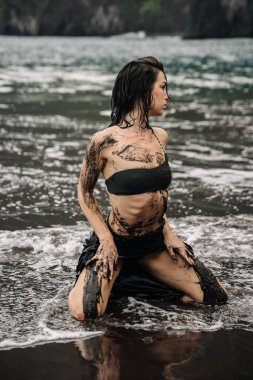 Suda diz çökmüş, çamurla süslenmiş kadın figürü, dalgalar nazikçe etrafta dolanıyor, doğanın, özgürlüğün ve kişisel yolculuğun temalarını anımsatıyor.