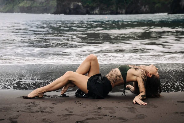 Siyah kumsalda bikinili kadın figürü, ayaklarına hafifçe dokunan dalgalar, doğal çevreyle uyum ve sükuneti somutlaştırıyor.