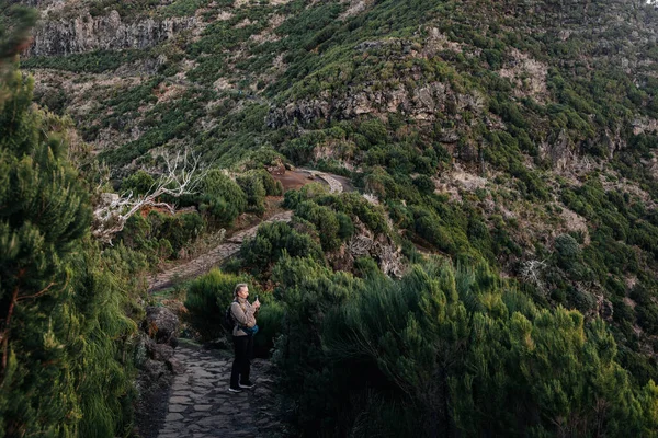 Dişi gezgin, canlı yeşillikler ve kayalık tepelerle çevrili dolambaçlı bir yolda duruyor. Huzurlu bir atmosferde büyüleyici manzaralar yakalıyor.