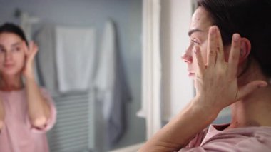 Banyodaki aynaya cilt bakımı yapan kadın.