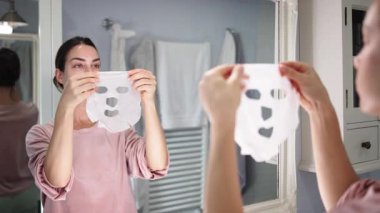 Banyo aynasında yüz maskesi tutan kadın.