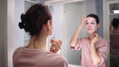 Banyo aynasına cilt bakımı yapan bir kadın.