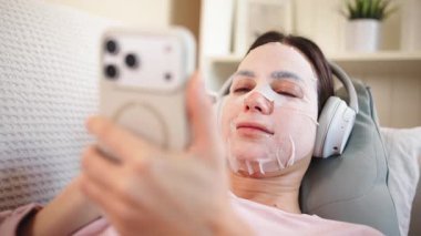 Kadın yüz maskesi ve telefonuyla dinleniyor.