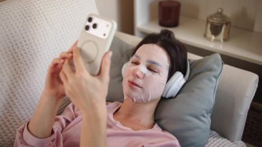 Kadın yüz maskesi ve telefonuyla dinleniyor.