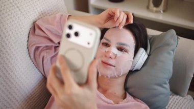 Kadın yüz maskesi ve telefonuyla dinleniyor.