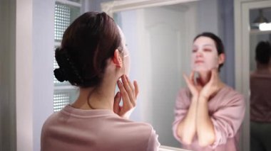 Genç bir kadın aynada yüzünü inceliyor..