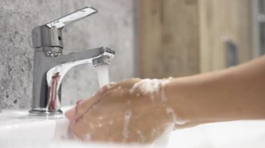 İnsan lavaboda akan suyun altında ellerini yıkıyor..