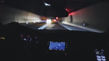 Modern bir aracın sürücü koltuğundan, uzun ve yapay olarak aydınlatılmış bir yol tünelinden geçerken...