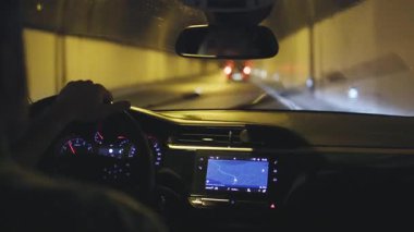 Modern bir aracın sürücü koltuğundan, uzun ve yapay olarak aydınlatılmış bir yol tünelinden geçerken...
