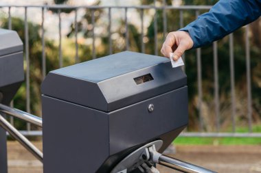 Mavi ceketli kişi açık hava girişinde bilet doğrulama makinesi kullanıyor. Modern toplu taşıma erişimi ve kullanıcı dostu teknoloji gösteriyor.