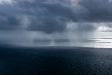 Fırtınalı okyanus sahnesinde karanlık bulutlar ve uzak yağmurlar doğanın gücünü ve güzelliğini büyüleyici bir deniz manzarasında yakalıyor.