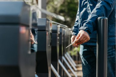 Mavi ceketli kişi otomatikleştirilmiş bilet kapısındaki ulaşım kartını tıklatıyor. Şehir içi ulaşımı ve modern ulaşım sistemlerini iş başında gösteriyor.