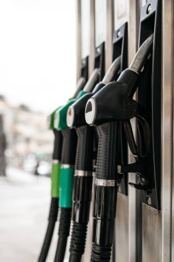Yakıt pompası nozüllerini yeşil ve siyah olarak yakından görmek, bir benzin istasyonundaki yakıt seçeneklerinin çeşitliliğini vurgulamak, kentsel bir arkaplana karşı ayarlamak