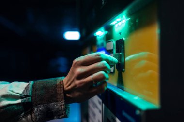 Bireyin eli düşük ışıklı bir alanda bir ödeme makinesi kullanıyor, teknoloji ve kentsel kolaylık ortamı ile etkileşimi vurguluyor