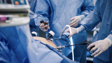 Mavi cerrahi giyimli tıp uzmanları, gelişmiş araçları kullanarak ve steril bir ortamda işbirliği sergileyerek, asgari düzeyde invazif bir operasyona girişiyor.