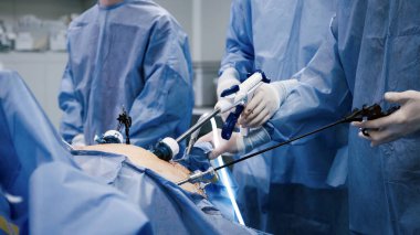 Mavi cerrahi giyimli tıp uzmanları, steril bir ortamda beceri ve işbirliği sergileyerek, asgari düzeyde invaziv bir operasyona girişiyor.