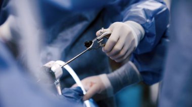 Mavi önlüklü sağlık çalışanı, temiz bir ameliyathanede hassas aletlerle tıbbi uzmanlık ve profesyonelliği vurgulayan bir cerrahi prosedür yürütüyor.