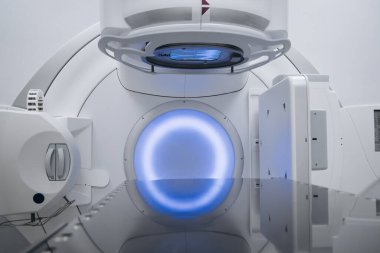 Onkoloji için gelişmiş doğrusal hızlandırıcı, parlak çizgilerle dizayn edilmiş ve yumuşak mavi ışıkla aydınlatılmış, klinik bir ortamda modern tıbbi teknolojiyi vurguluyor.