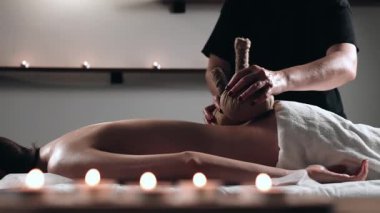 Kadın derisine bitkisel bolus torbalarıyla Ayurveda Masaj Terapisti. Masör kadın vücuduna nazikçe şifalı bitki torbaları bastırıyor. Sıcak bitkisel top masaj vücut tedavisi.