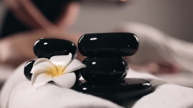 Masaj masasındaki kadın kaplıcada elinde çiçekli siyah taşlar var..