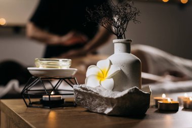 Spa ortamında çiçek, gerekli yağ ve mumlarla süslü bir vazo sergileniyor. Masaj terapisi için sakin bir ortam yaratıyor.