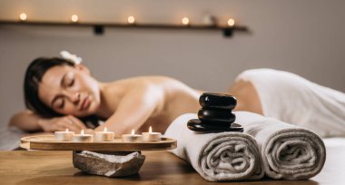 Kadın, yumuşak havlular, parlayan mumlar ve pürüzsüz taşlar ile çevrili sakin bir spa ortamında rahatlatıcı bir masajdan hoşlanır.