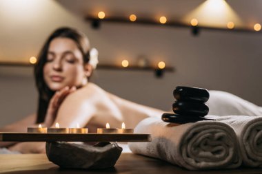 Spa ortamı, mumlar, pürüzsüz taşlar ve pelüş havlularla çevrili, rahatlatıcı bir masajdan hoşlanan bir kadının rahatlamasını ve kendine bakmasını sağlıyor.