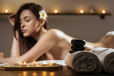 Sakin bir spa ortamında, mumlar, pürüzsüz taşlar ve pelüş havlularla çevrili, rahatlatıcı bir masaj alan bir kadın sergileniyor.