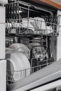 Çağdaş bulaşık makinesi temiz bulaşık ve çatal bıçaklarla dolu, mutfak hijyeni ve konforunu korumak için pratik tasarımı ve verimliliği vurguluyor.