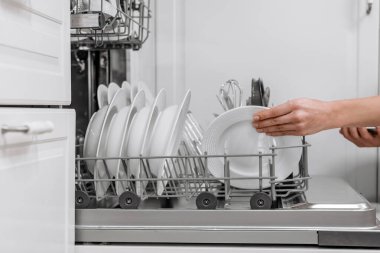 Temiz beyaz tabaklar bulaşık makinesine yerleştiriliyor. Temizliği ve verimli bulaşık yıkamayı ön plana çıkaran düzenli bir mutfak alanı vurgulanıyor.