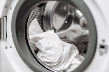 Çamaşır makinesinin varilinde çamaşır yıkama, kumaş dokusunu ve cihazın parlak tasarımını vurgulama, temizlik ve modern kolaylık hissi yaratma,