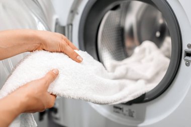 Bireysel çamaşır makinesinden yumuşak beyaz havluyu çıkarmak, çamaşır rutinini vurgulamak ve günlük yaşamda yeni, temiz tekstil ürünlerinin önemini vurgulamak.