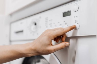 Çamaşır makinesini çalıştıran bir elin yakın çekimi, kontrol panelini düğmeler ve dijital ekran ile ayarlamak, modern ev aletleri ve kullanılabilirliği vurgulamak