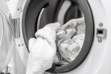 Çamaşır makinesinin kapısından sarkan havlu, içinde temiz çamaşırlar, günlük ev işlerindeki temizliğin önemini vurguluyor.