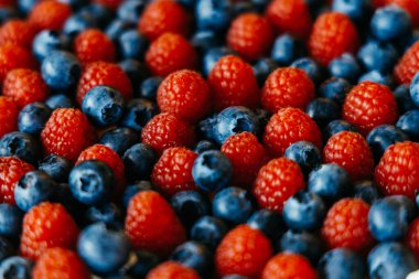 Taze ahududu ve yaban mersinlerinin renkli bir görüntüsü, zengin dokularını ve canlı renklerini vurguluyor, sağlıklı tarifler ve yemek fotoğrafçılığı için ideal.