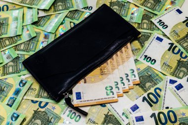 Avro banknotları ve bozuk paralarla çevrili siyah cüzdan, finans, zenginlik ve ekonomik işlemler temaları gösteren düz bir zemin üzerinde