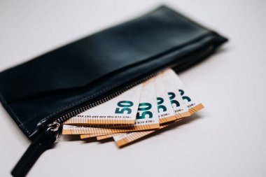Fermuarsız siyah deri cüzdan, temiz ve modern bir ortamda finans, güvenlik ve kişisel zenginlik temalarını vurgulayarak, birden fazla 50 banknot sergiliyor.