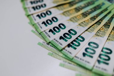 A fan of hundred euro banknotes displayed on a white surface, highlighting detailed designs and colors, representing financial transactions and economic concepts