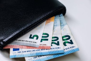 Siyah cüzdanda beş, yirmi ve yirmi beş banknot da dahil olmak üzere çeşitli banknotlar yer alıyor, bunlar kişisel finans ve ekonomi yönetimini gösteriyor