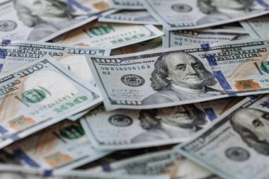 Düz bir yüzeye dizilmiş sayısız yüz dolarlık banknotların yakın plan görüntüsü detaylı doku ve renkleri vurguluyor, bolluğu ve ekonomik başarıyı simgeliyor
