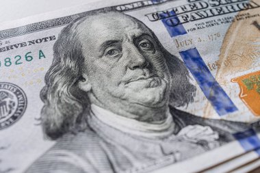 Yüz dolarlık banknotun yakın plan görüntüsü, detaylı portre, güvenlik unsurları ve canlı renkler, zenginlik ve ekonomik işlemleri simgeliyor.