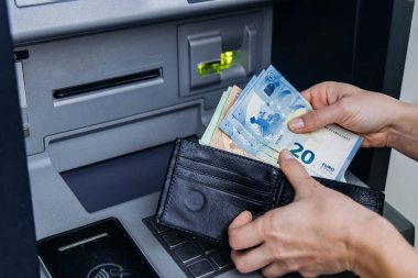 Bankamatiği para çekmek için kullanan, içinde avro banknotları olan siyah bir cüzdan tutan, dijital bankacılık ortamında fonlara ulaşmanın kolaylığını vurgulayan kişi