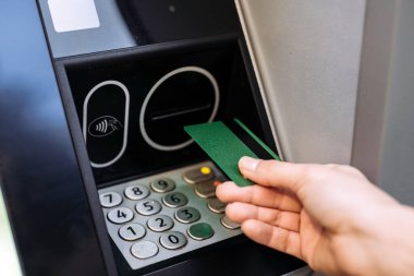 Bireysel olarak ATM makinesine yeşil banka kartı yerleştiriliyor, klavye ve kart okuyucu görünür, finans hizmetlerine erişimin kolaylığını vurguluyor