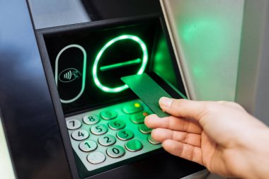 Bireyin eli ATM 'ye kart sokuyor, aydınlatmalı tuş takımı ve ekran işlem seçeneklerini gösteriyor, kullanıcı dostu bankacılık deneyimini vurguluyor