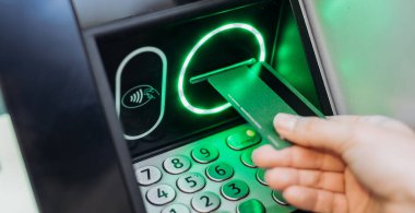 Bireyin eli bankamatiğe bir banka kartı koyuyor, aydınlatma düğmeleri ve yeşil ışıkları olan, modern bankacılık teknolojisi ve kullanıcı deneyimini temsil eden