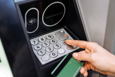 Genç kadın ATM makinesiyle etkileşime giriyor, banka kartı tutarken tuş takımına basıyor, dijital bankacılık ve finansal işlemlerin kolaylığını gösteriyor