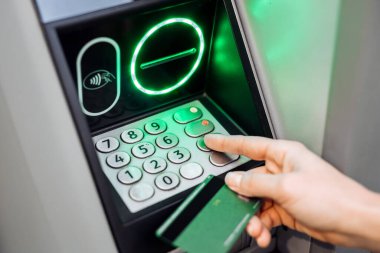 Kullanıcının eli ATM tuş takımı ile meşgul, yeşil kartı tutarken tuşlara basıyor, bankacılık teknolojisi ve finans hizmetleri ile etkileşimi gösteriyor
