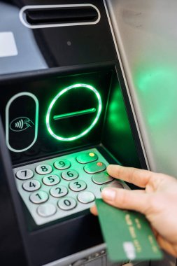 Şahıs bir ATM makinesi kullanıyor, banka kartı tutarken tuşlara basıyor, yeşil ışıklarla aydınlatılıyor, modern bankacılık kolaylığını temsil ediyor.